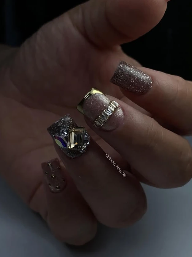 Uñas con glitter plateado, cristales y detalles metálicos dorados